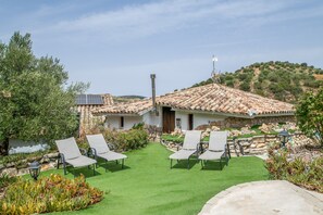 A villa with a tiled roof, a stone wall, and a grassy lawn with two lounge chairs.