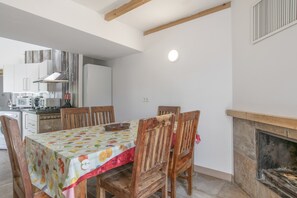 A dining area with a table covered in a fruit-patterned tablecloth, wooden chairs, and a fireplace.