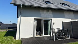 Una casa moderna con techo inclinado, antena parabólica y un patio con sillas.