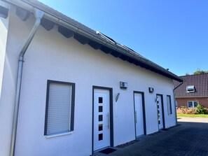 Ein Gebäude mit weißer Fassade, mehreren Türen und Fenstern mit Rollläden.