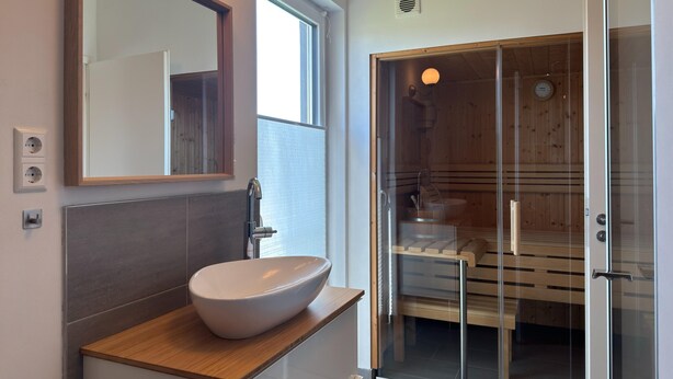 Un baño moderno con un espejo grande, un lavabo sobre encimera, una cabina de ducha de vidrio y una zona de baño de madera.