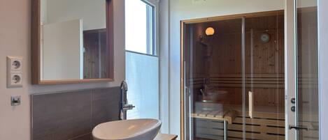A modern bathroom with a large mirror, a vessel sink, a glass shower enclosure, and a wooden bath area.