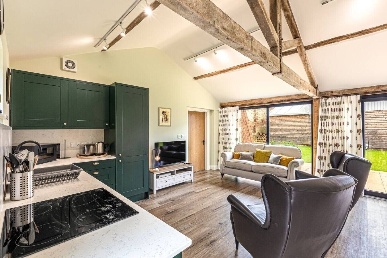 A kitchen with a stove, microwave, and green cabinets, a dining area with a table and chairs, and a living room with a sofa and a TV.