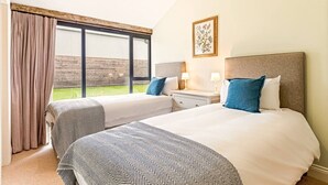 Een hotelkamer met twee bedden, een raam met gordijnen, een nachtkastje met lampen en een ingelijste foto aan de muur.