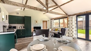 Een eetgedeelte met een tafel voor vier personen, een keuken met groene kasten en een zithoek met een bank en stoelen.