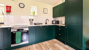 Een keuken met groene kastjes, een magnetron, een spoelbak en een klok aan de muur.