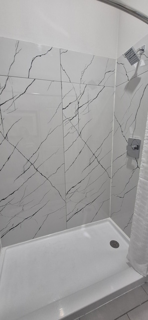 A shower with a white marble wall and a white bathtub. - Platinum Inn Copperfield (Houston)