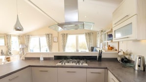 A modern kitchen with a central island, built-in appliances, and large windows. - The Stables (Pwllheli)