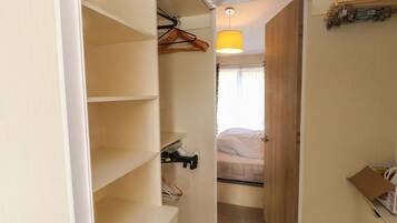 Un pasillo estrecho que conduce a un dormitorio con una cama, una lámpara colgante y un armario con estantes.