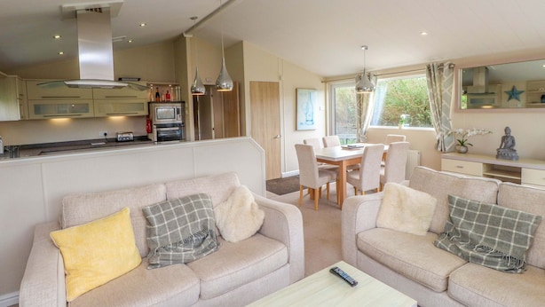A modern living room with a sofa set, a dining table, and a kitchen area with appliances. - The Stables (Pwllheli)