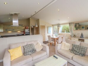 A modern living room with a sofa set, a dining table, and a kitchen area with appliances. - The Stables (Pwllheli)