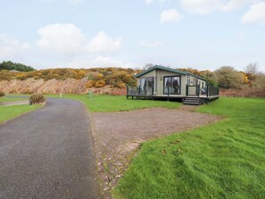 A single-story mobile home with a paved driveway leading to a grassy area. - The Stables (Pwllheli)