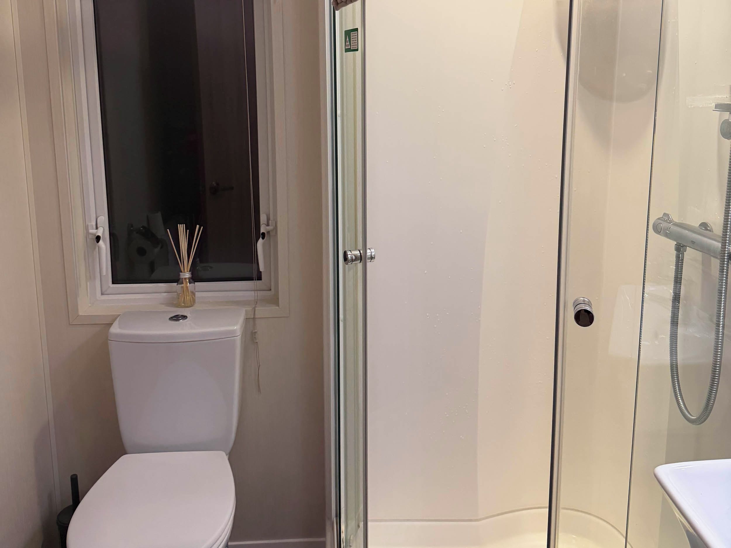 A bathroom with a toilet, a glass-enclosed shower, and a window above the toilet.