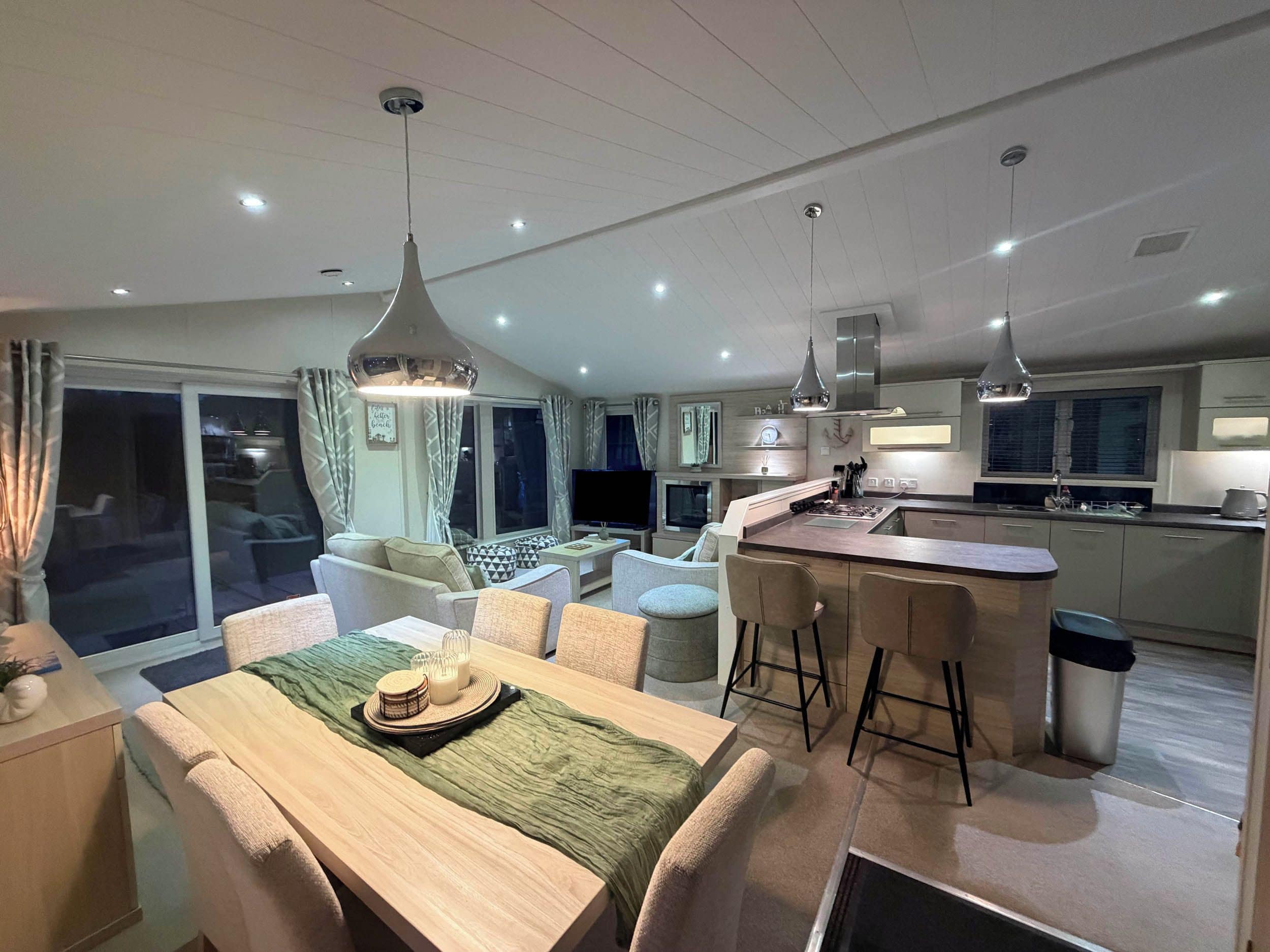 A modern kitchen with a central island, dining area with a table set for two, and a living room with a sofa and TV.
