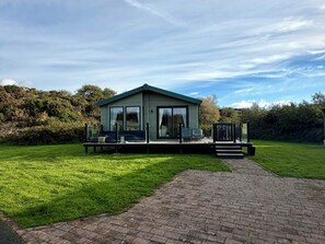 A modern, single-story building with a flat roof, large windows, and a deck area with outdoor seating. - The Stables (Pwllheli)