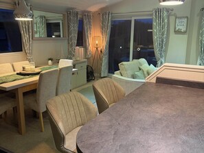 A dining area with a table and chairs, a lamp, and a view through a window. - The Stables (Pwllheli)