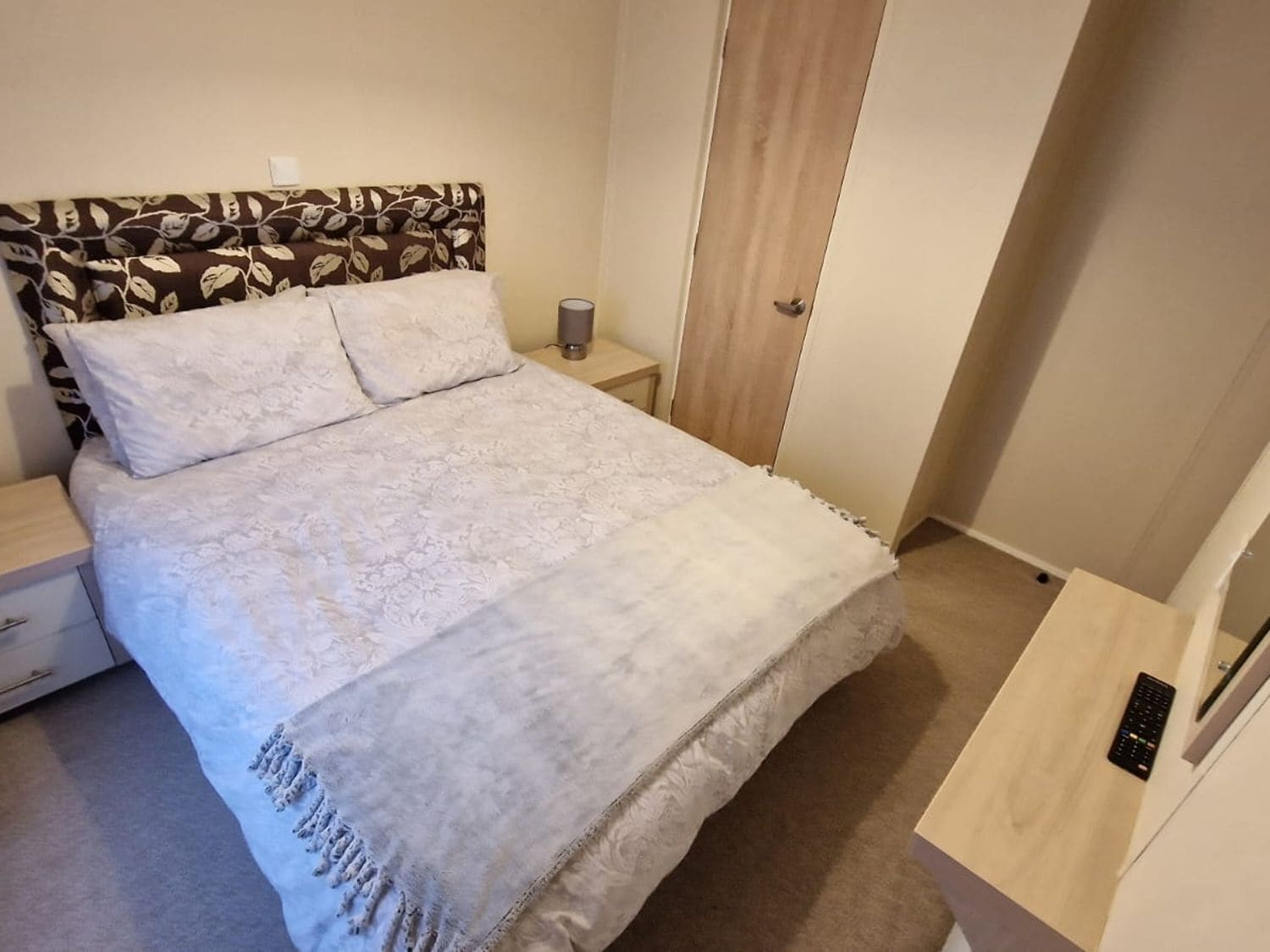 A bedroom with a bed, a nightstand, a lamp, a wardrobe, and a control panel.