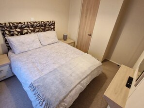 A bedroom with a bed, a nightstand, a lamp, a wardrobe, and a control panel. - The Stables (Pwllheli)