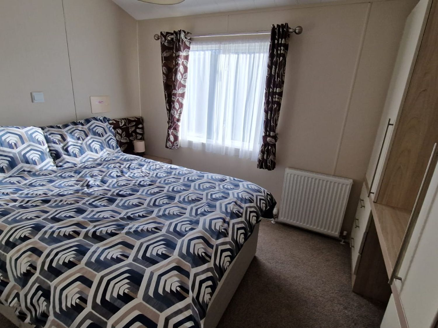 Un dormitorio con una cama, una ventana con cortinas, un radiador y una puerta.