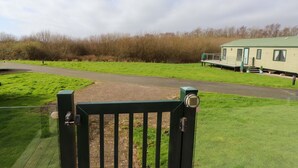 A gated entrance to a park with a pathway leading to a mobile home. - The Stables (Pwllheli)