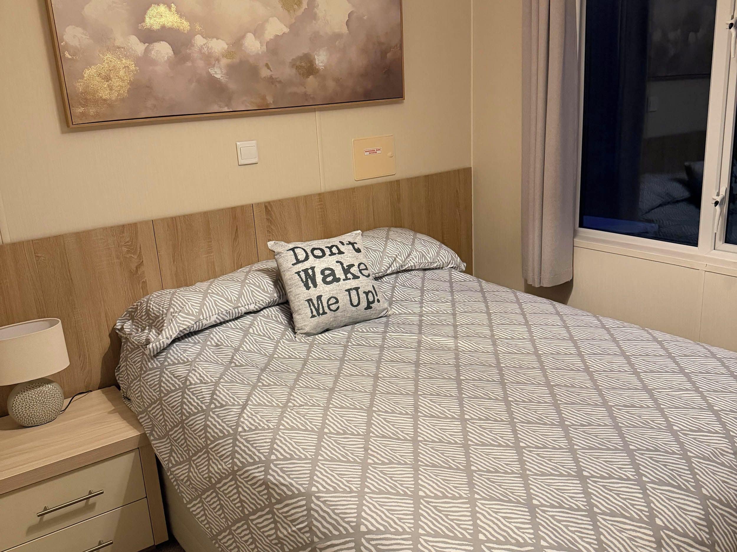 A bedroom with a bed, a nightstand, a lamp, a wall art piece, and a window with curtains.