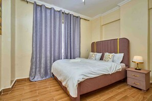 Ein Schlafzimmer mit einem Bett, einem Nachttisch, einer Lampe und einem Fenster mit Vorhängen.