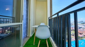 Un balcón con una silla blanca, una mesita y vistas a edificios.