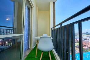 Ein Balkon mit weißem Stuhl, einem kleinen Tisch und Blick auf Gebäude.
