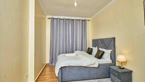 Un dormitorio con cama, cortinas, mesita de noche y lámpara.