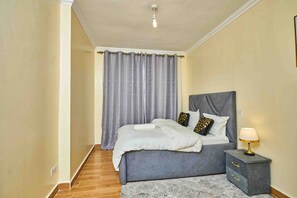 Ein Schlafzimmer mit Bett, Vorhängen, Nachttisch und Lampe.