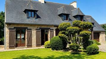 Une grande maison à la façade en pierre, dotée de nombreuses cheminées et d’une pelouse bien entretenue.