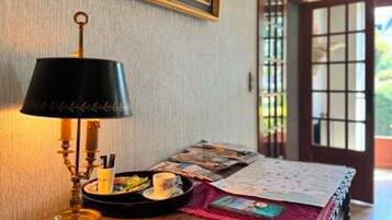 Une pièce avec un bureau, une lampe, un tableau encadré et une vue sur l’extérieur, visible à travers une porte.