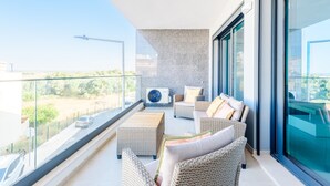A balcony with wicker furniture, a large window, and a view of a road. - Alvor Ria Retreat House (Alvor)
