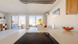 A modern kitchen with a built-in stove, a dining area with a table and chairs, and a view of buildings through large windows. - Alvor Ria Retreat House (Alvor)