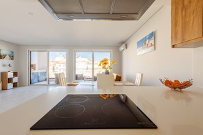 A modern kitchen with a built-in stove, a dining area with a table and chairs, and a view of buildings through large windows. - Alvor Ria Retreat House (Alvor)