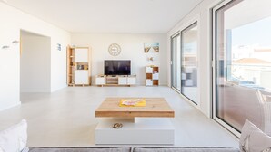 A modern living room with a flat-screen TV, a coffee table, and a large window. - Alvor Ria Retreat House (Alvor)