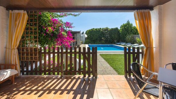 A covered patio with a view of a swimming pool, a wooden fence, and a chair. - Galindo Apartments: Shared Pool, Family-Only Accommodation (Fuente del Gallo)