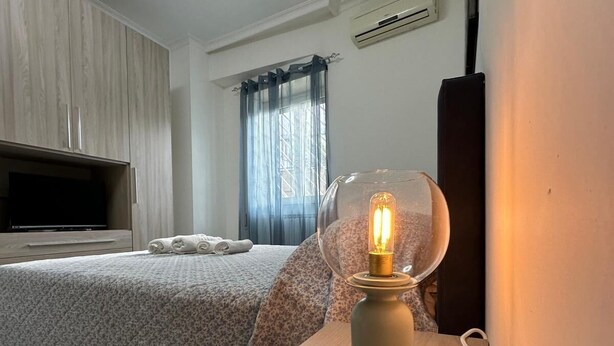 A bedroom with a bed, a television, a wall-mounted air conditioner, and a table with a lamp. - Pigneto Metro Station, Line C, ground floor: spacious bedroom, kitchen, and bathroom. (Roma)