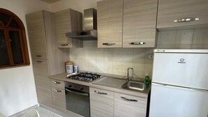 A modern kitchen with light wood cabinets, a stainless steel range hood, a built-in oven, a sink, and a white refrigerator. - Pigneto Metro Station, Line C, ground floor: spacious bedroom, kitchen, and bathroom. (Roma)