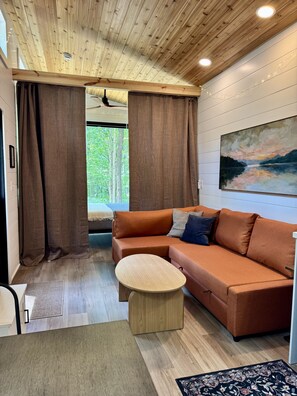A modern living room with a wooden ceiling, a brown sofa, a round coffee table, and a painting on the wall.