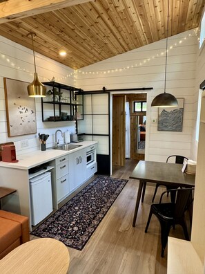 A modern kitchen with white cabinets, a wooden ceiling, and string lights.