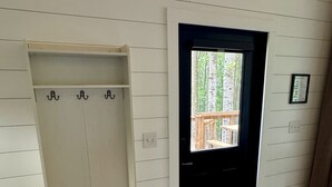 Ein Zimmer mit weißer Holzwand, einer schwarzen Tür, einem Kleiderständer, einer Bank und einer Fußmatte.