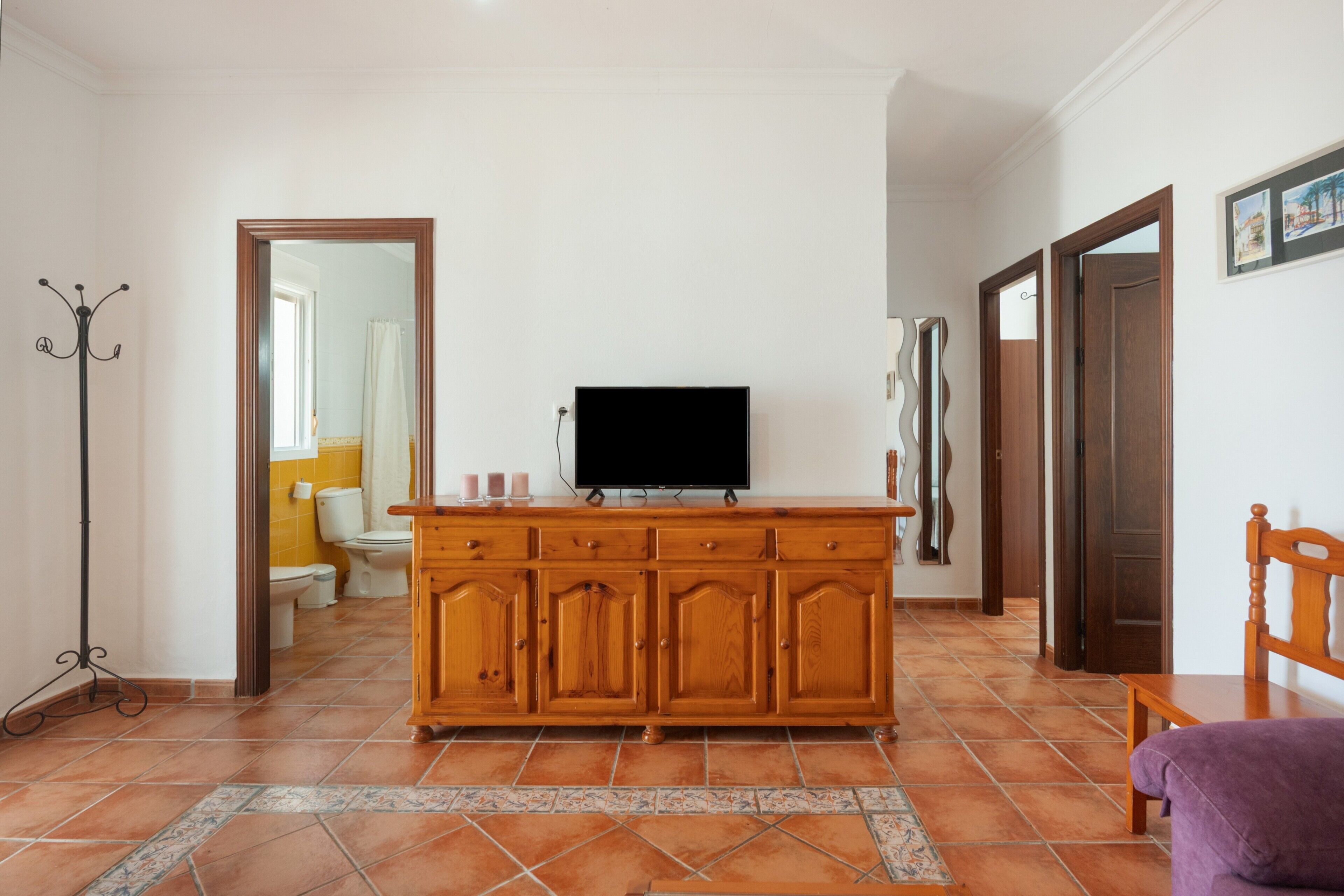 Una sala de estar con un aparador de madera, un televisor, un perchero y una silla.