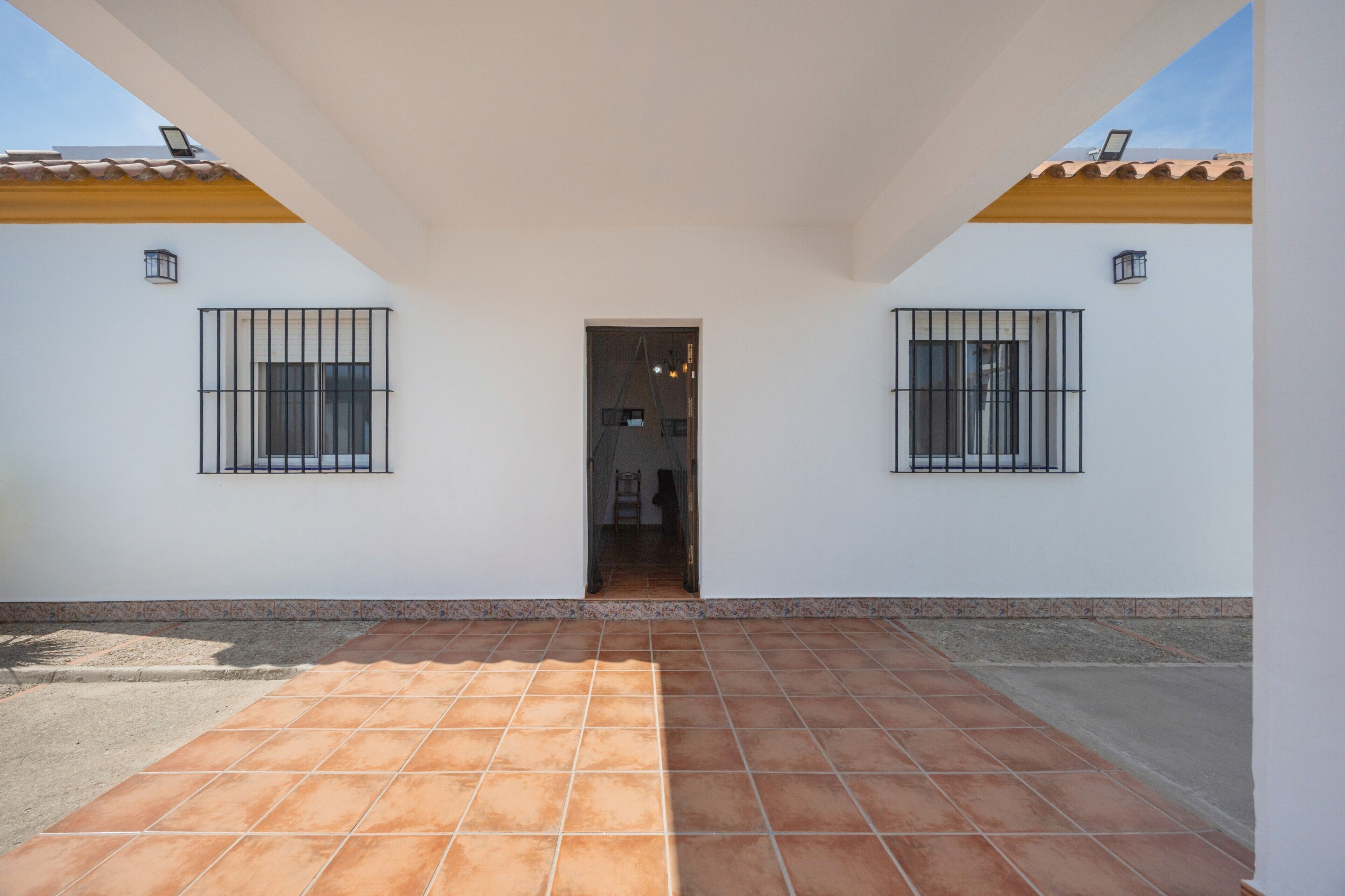 A building with a tiled patio, two windows with metal bars, and a door leading to an interior.