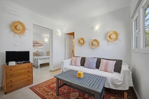 Una habitación con sofá, televisión, cómoda de madera y alfombra roja estampada.