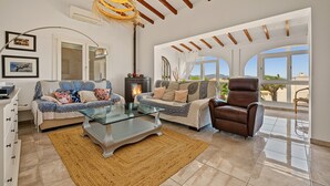 Een ruime woonkamer met een open haard, twee banken, een glazen salontafel en een lederen fauteuil.