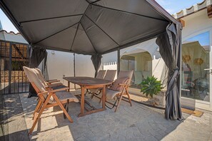 Pátio externo com mesa e cadeiras sob uma tenda grande.