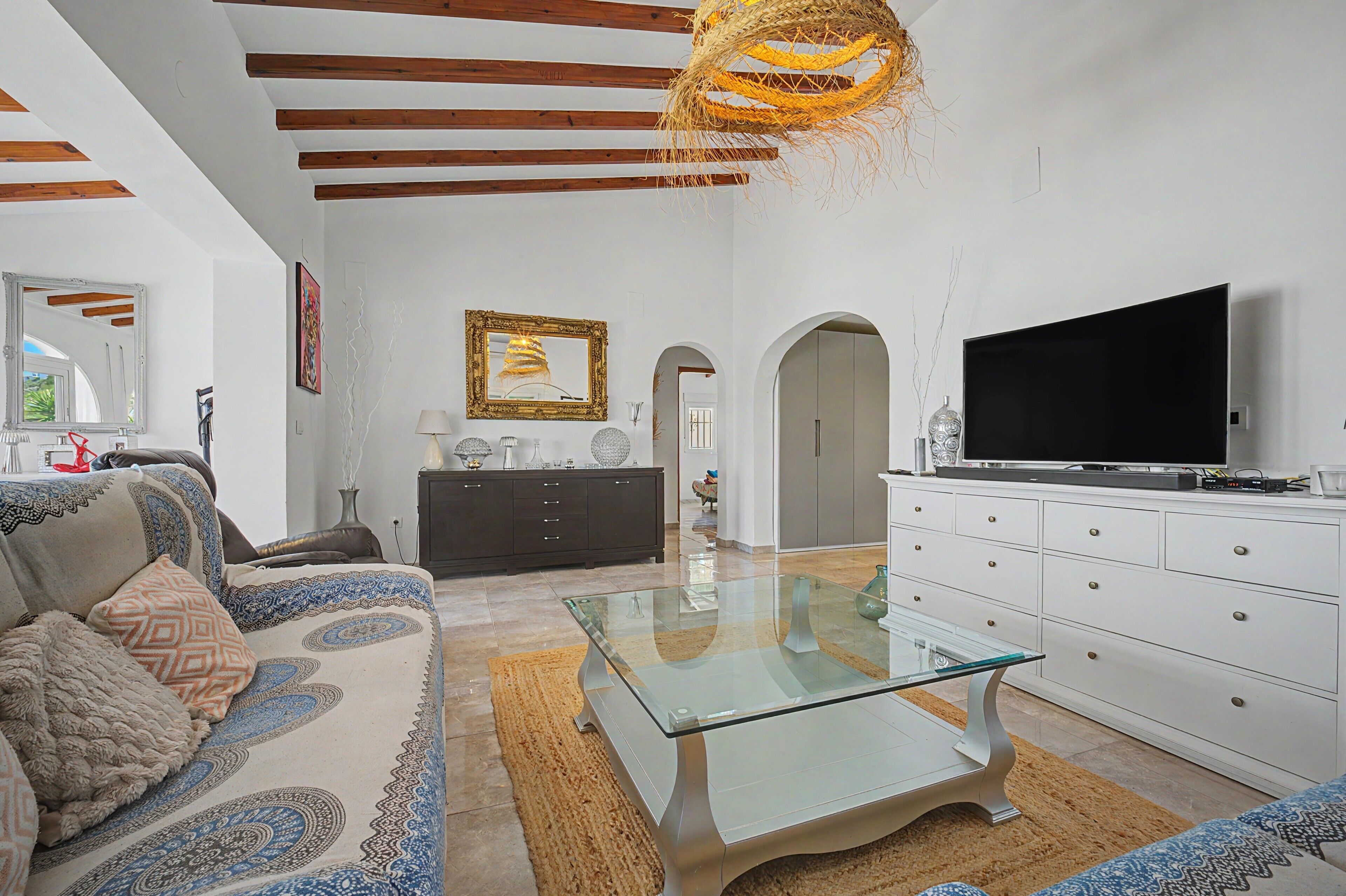 A modern living room with a sofa, a glass coffee table, a television, and a decorative mirror.