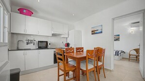 Een moderne keuken met witte kasten, een eettafel met houten stoelen en een magnetron.