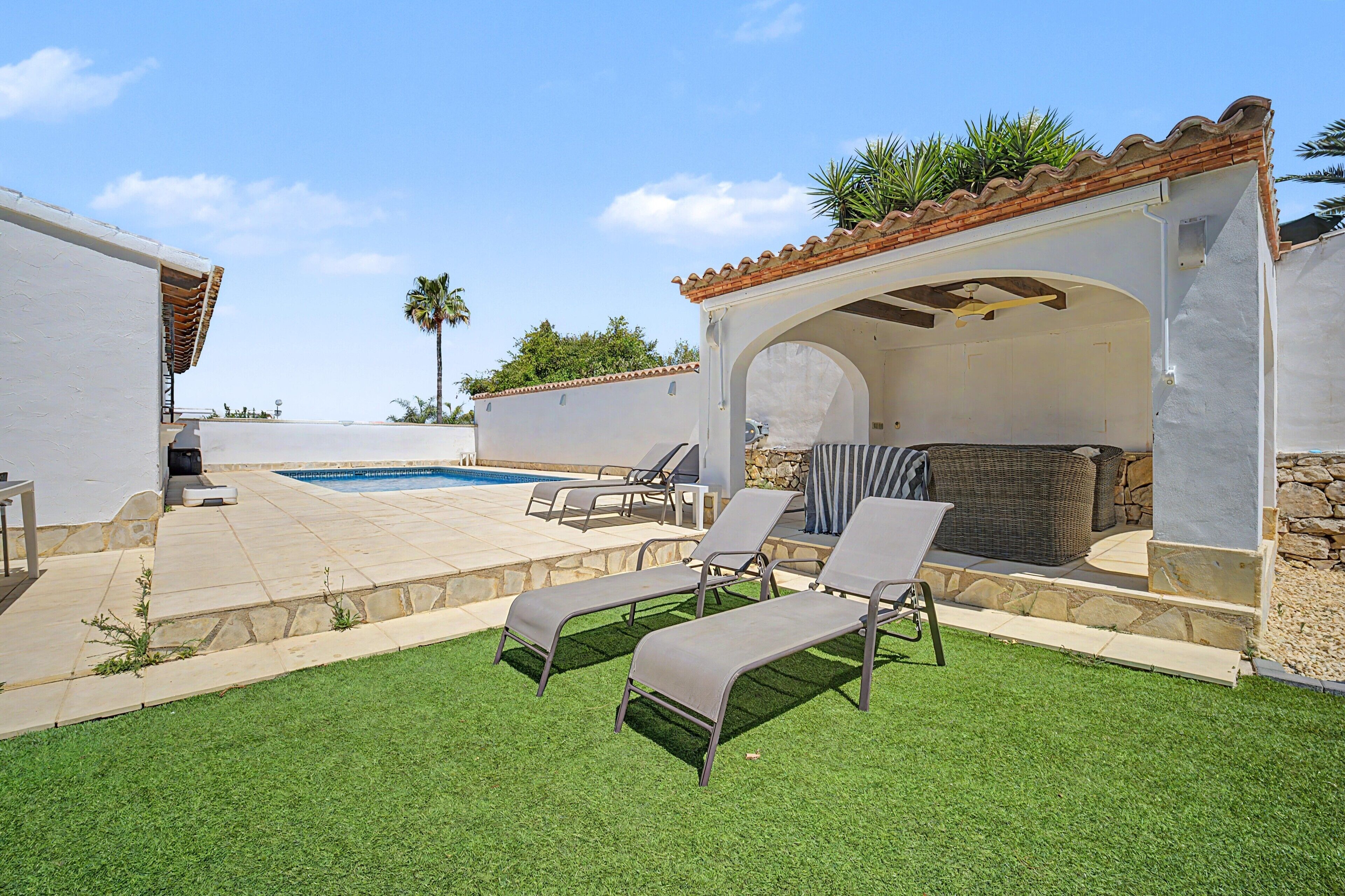 A poolside area with lounge chairs, a covered seating area, and a view of the pool.